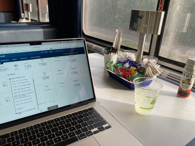 Laptop of dining table with drink next to picture window.